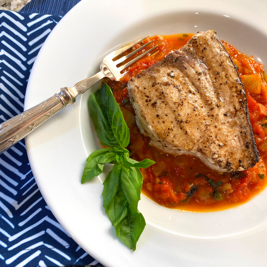 Grilled swordfish steak on tomato sauce with fresh basil on a white plate, Cooking with Barbara recipe