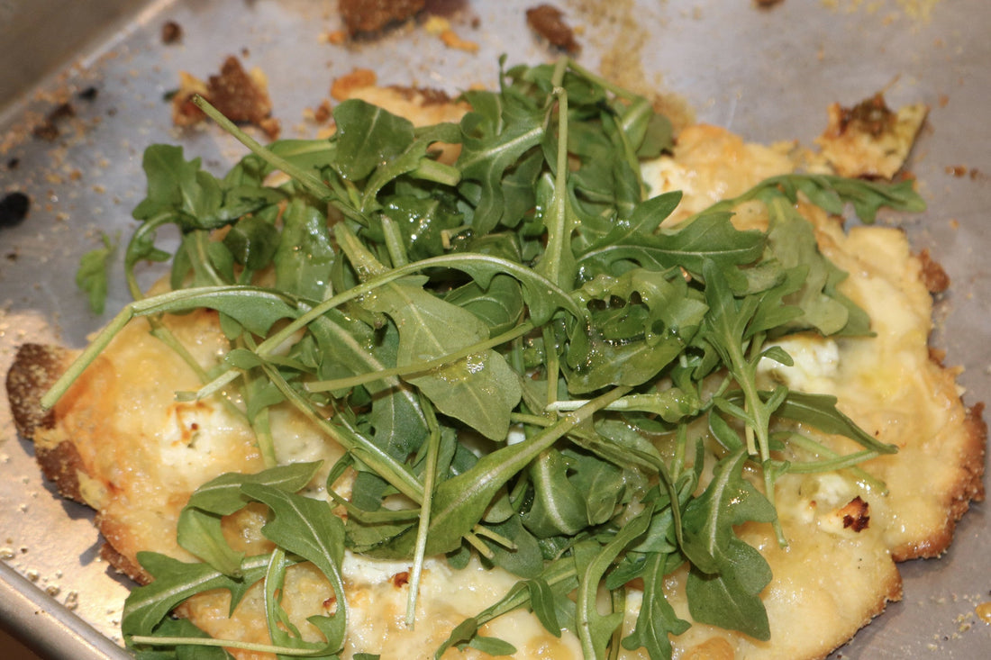 Homemade pizza topped with a generous handful of fresh arugula in a cast iron pan