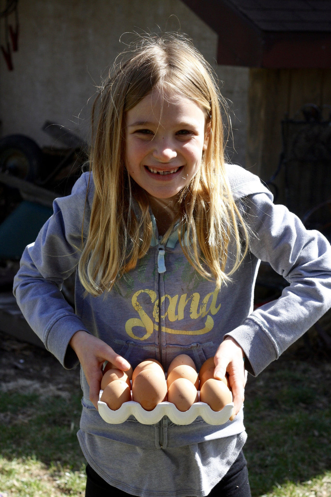 Young girl smiling and holding a ceramic egg tray with fresh brown eggs from the backyard chicken coop