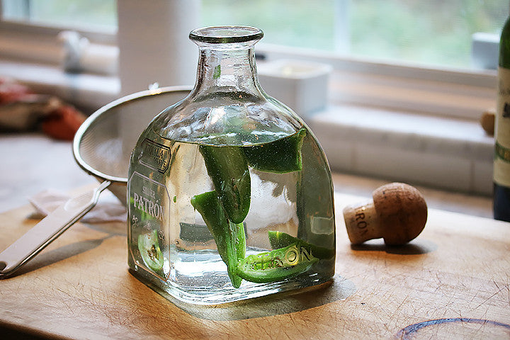 Patron Silver tequila bottle with jalapeño slices infusing on a wooden cutting board for jalapeño margaritas