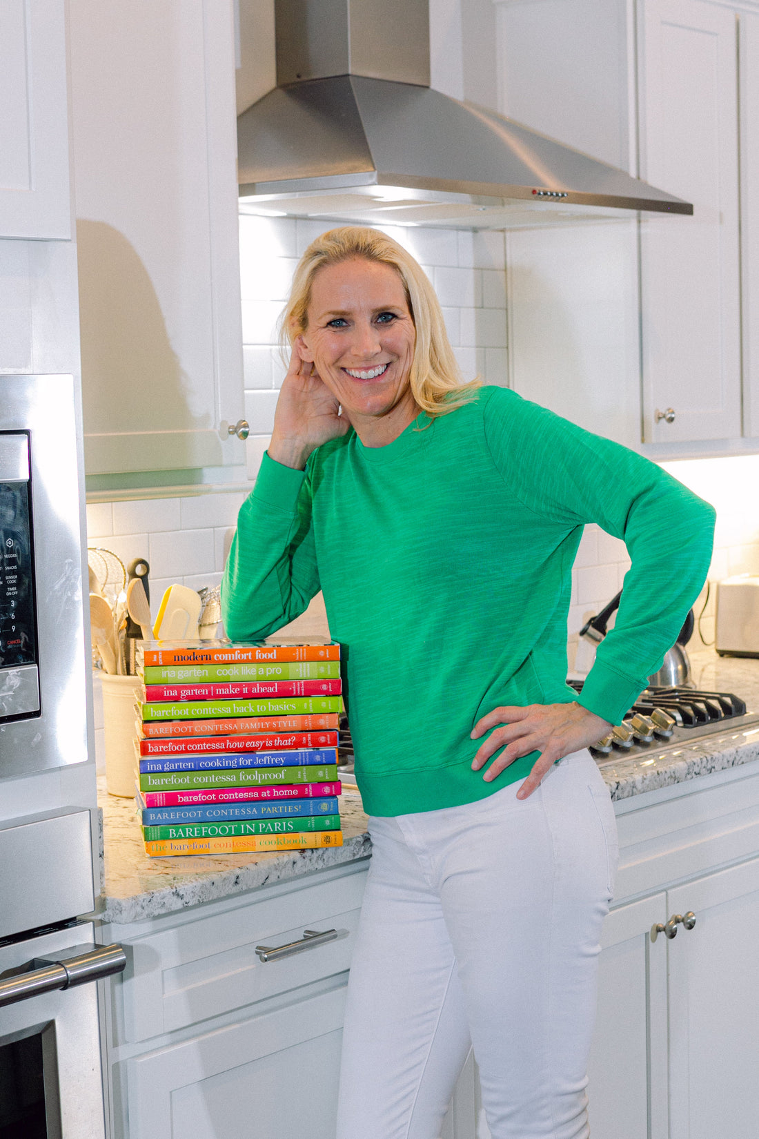 Cassandra standing in a white kitchen next to a stack of Ina Garten Barefoot Contessa cookbooks for Mother's Day