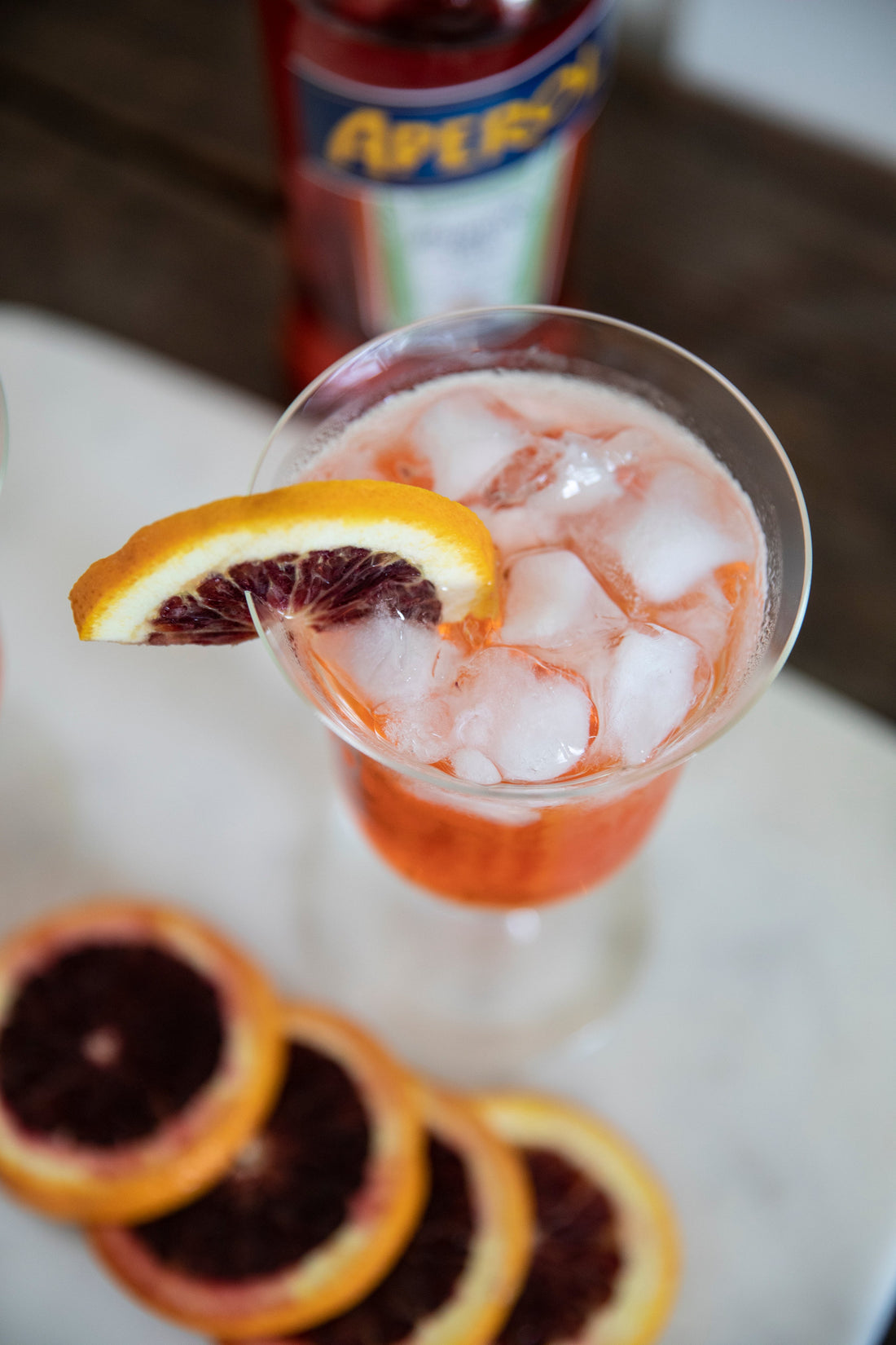 Ina Garten's Aperol Spritzer with a blood orange slice on ice in a stemmed glass, Aperol bottle in background