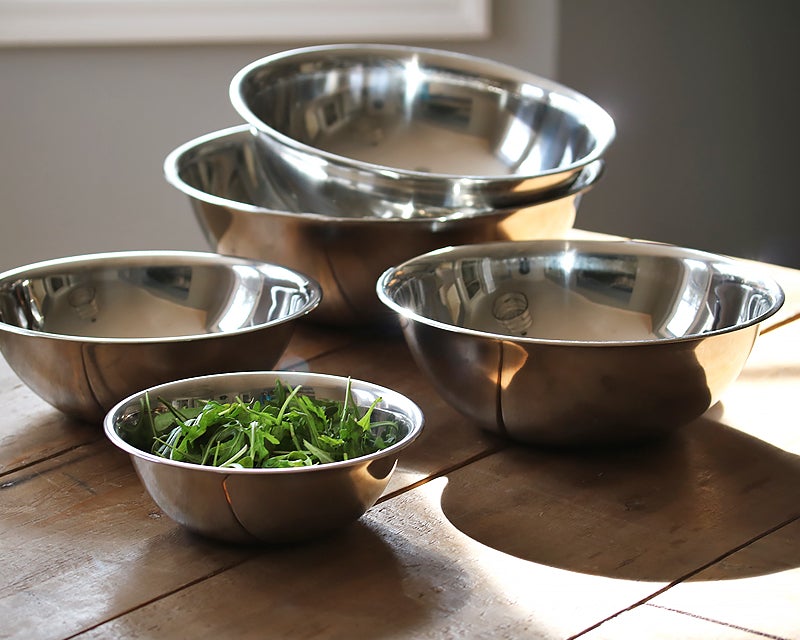 Set of five polished stainless steel mixing bowls in graduated sizes on a wooden table, top kitchen essentials for 2022