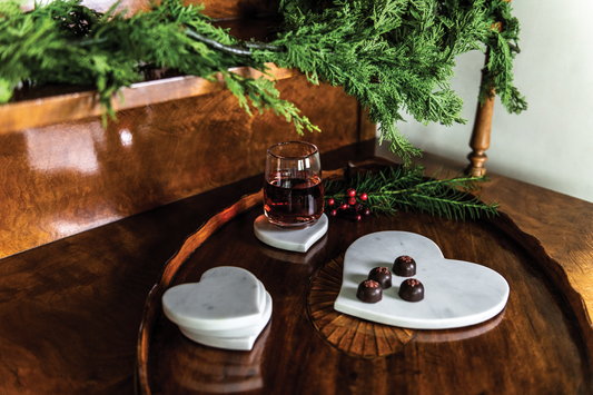 Heart-shaped marble coasters with dark chocolates and red wine on a wood tray with pine greenery, Valentine's Day arrivals