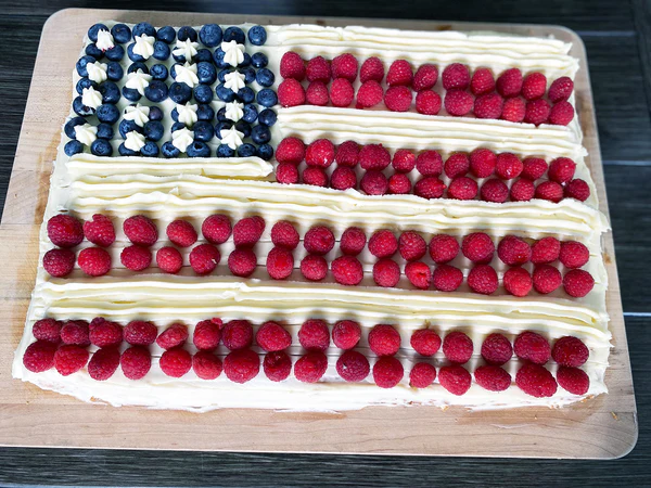 Fourth of July flag cake decorated with blueberries, strawberries, and raspberries on white frosting