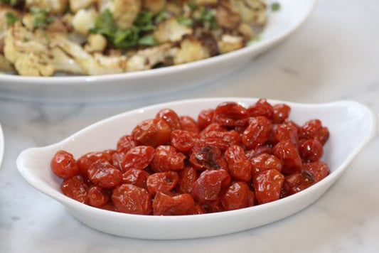 Roasted cherry tomatoes in a white oval dish with roasted cauliflower in background, easy weeknight side