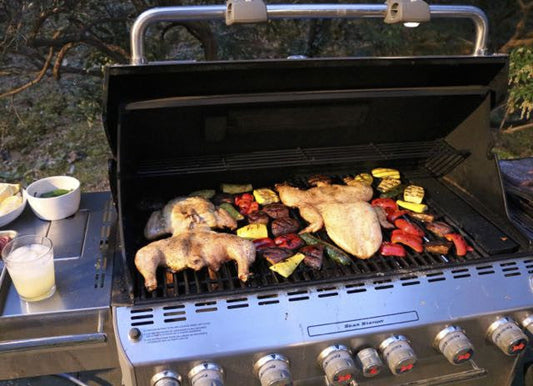 Whole Argentine-style chicken and colorful vegetables grilling on an open gas barbecue