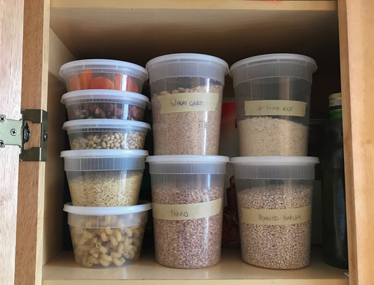 Organized kitchen pantry with labeled deli containers of wheat germ, jasmine rice, farro, pearled barley, pasta, and legumes