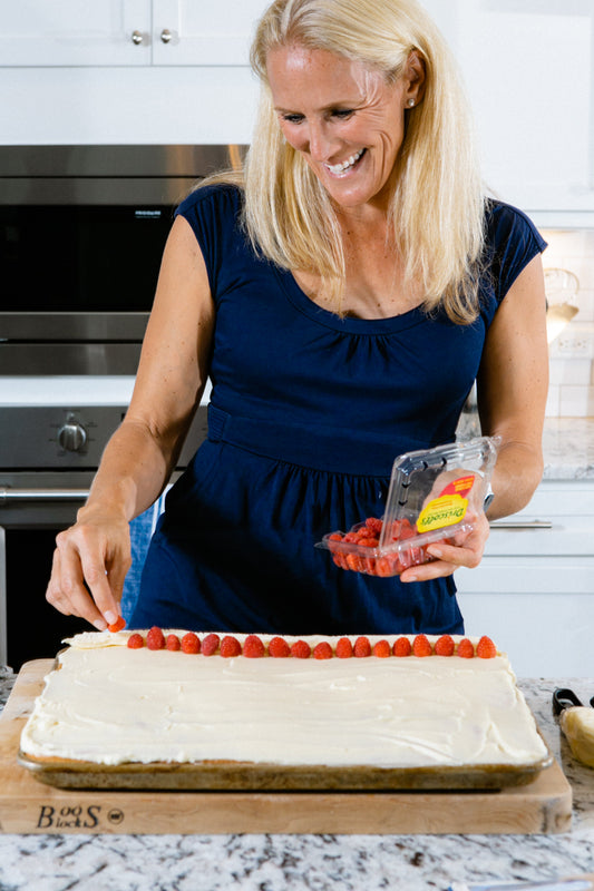 Cassandra decorating a large Memorial Day sheet cake with white frosting and a row of fresh strawberries