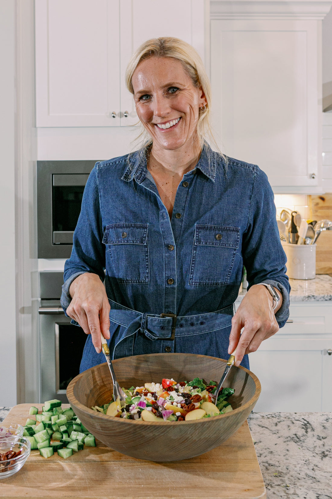 Cassandra tossing an apple harvest salad with feta and vegetables in a large wooden bowl