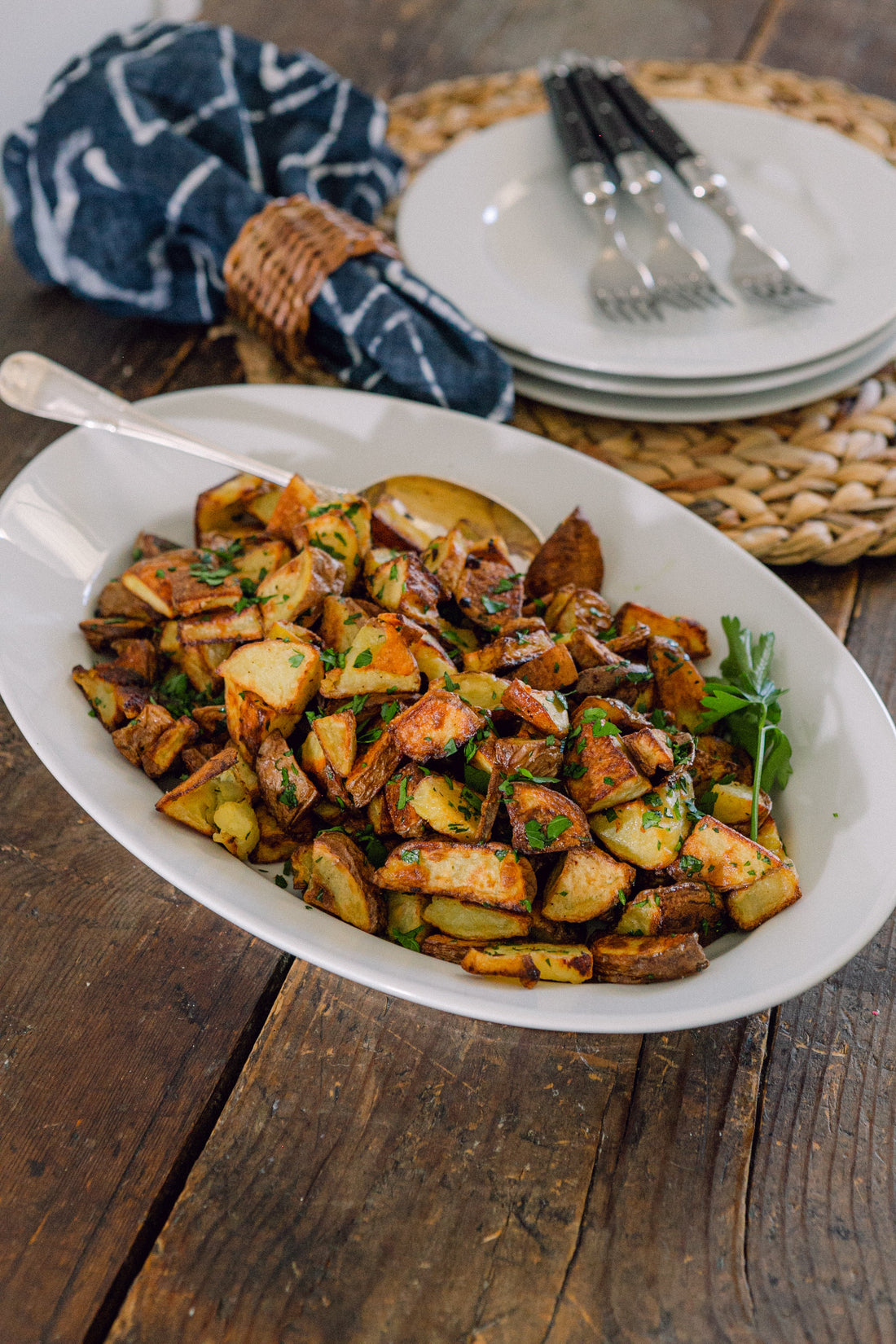 Ina Garten's Garlic Roasted Potatoes on a white oval serving platter with fresh parsley on a rustic wood table