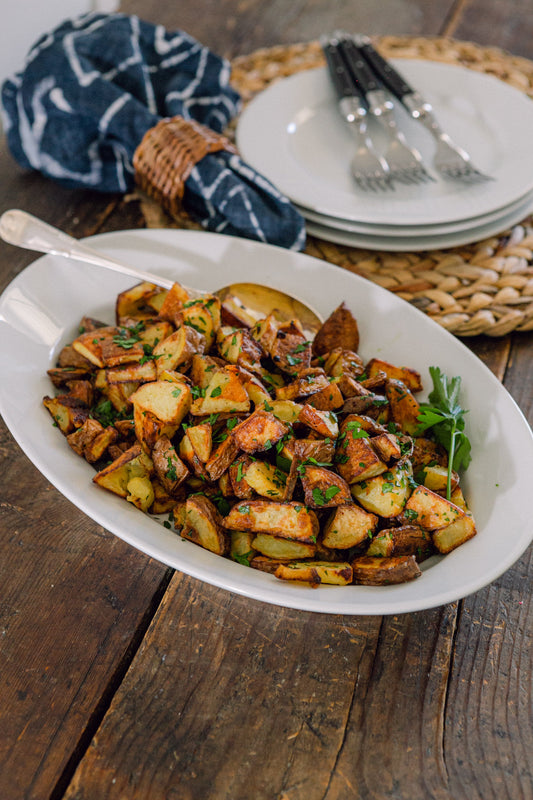 Ina Garten's Garlic Roasted Potatoes on a white oval serving platter with fresh parsley on a rustic wood table