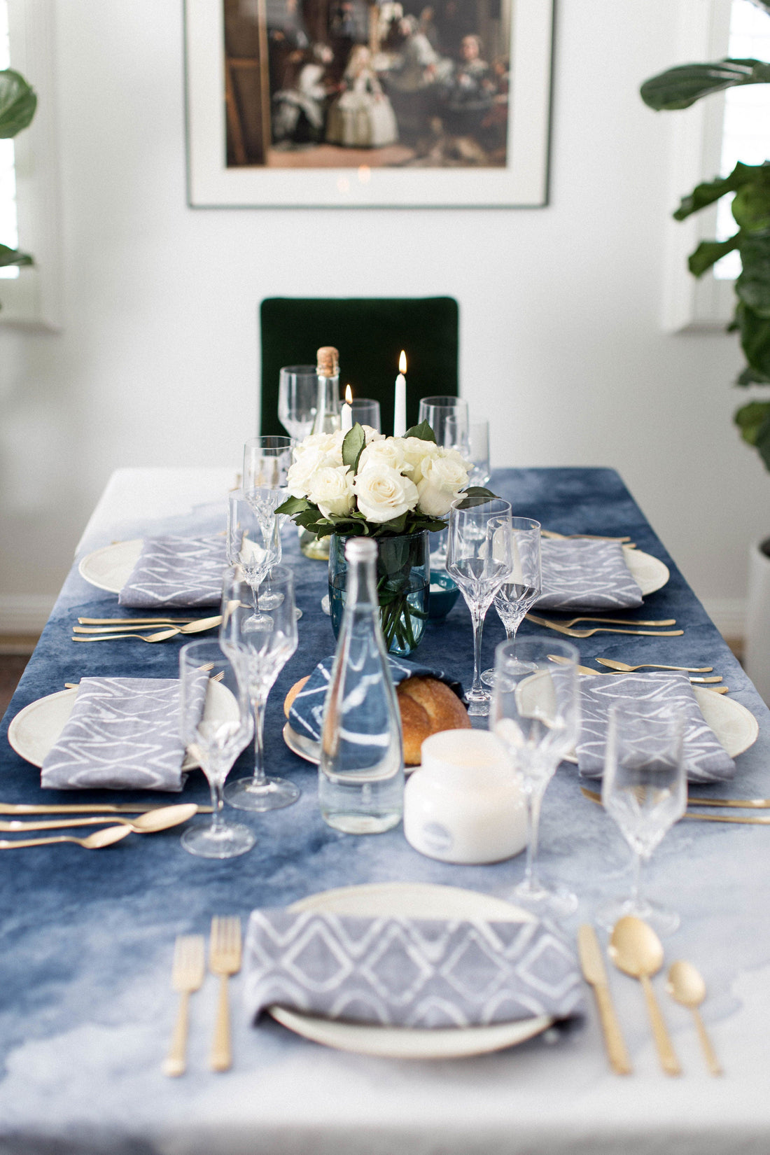 Formal dinner table set with blue cloud-print tablecloth, geometric napkins, gold flatware, crystal champagne flutes, and white roses