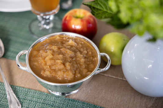 Ina Garten's Homemade Applesauce in a jar with fresh apples on a countertop