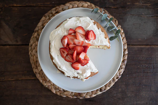 Ina Garten's Strawberry Country Cake topped with whipped cream and fresh sliced strawberries on a woven placemat
