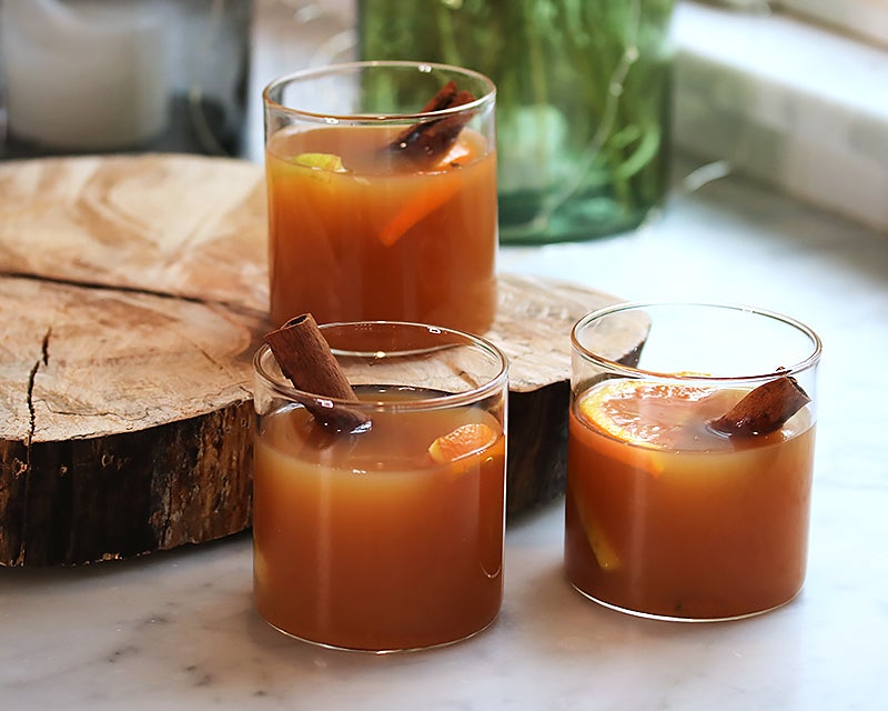Three warm spiced cocktails with cinnamon sticks and orange slices in glass tumblers, favorite barware recipes