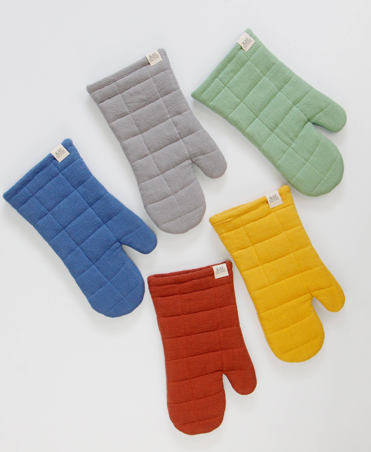 Five quilted cotton oven mitts in blue, grey, sage green, mustard yellow, and rust red on a white background
