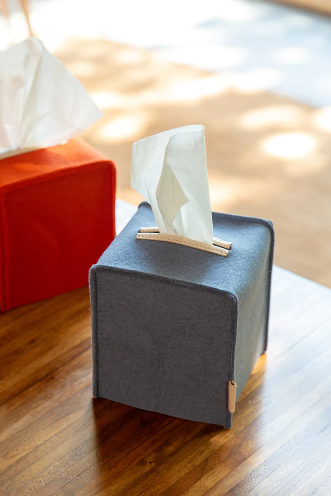 Graf Lantz grey wool felt tissue box cover with leather tab detail on a wood surface, red felt cover behind it