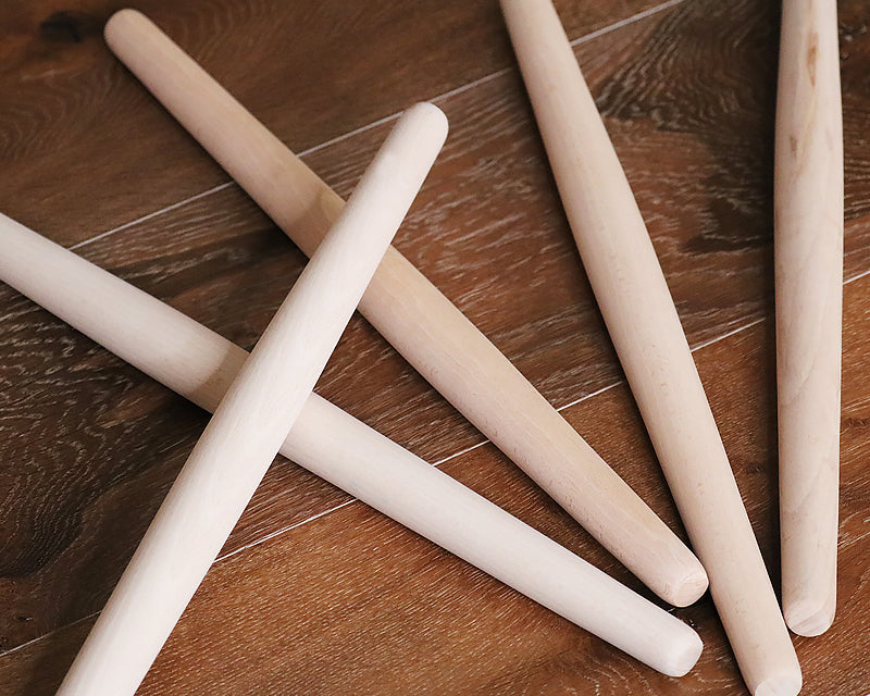 Five natural wood French rolling pins arranged on a dark wood surface