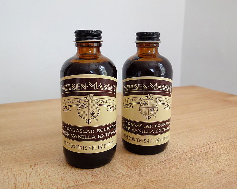 Two bottles of Nielsen-Massey Madagascar Bourbon Pure Vanilla Extract on a wooden cutting board