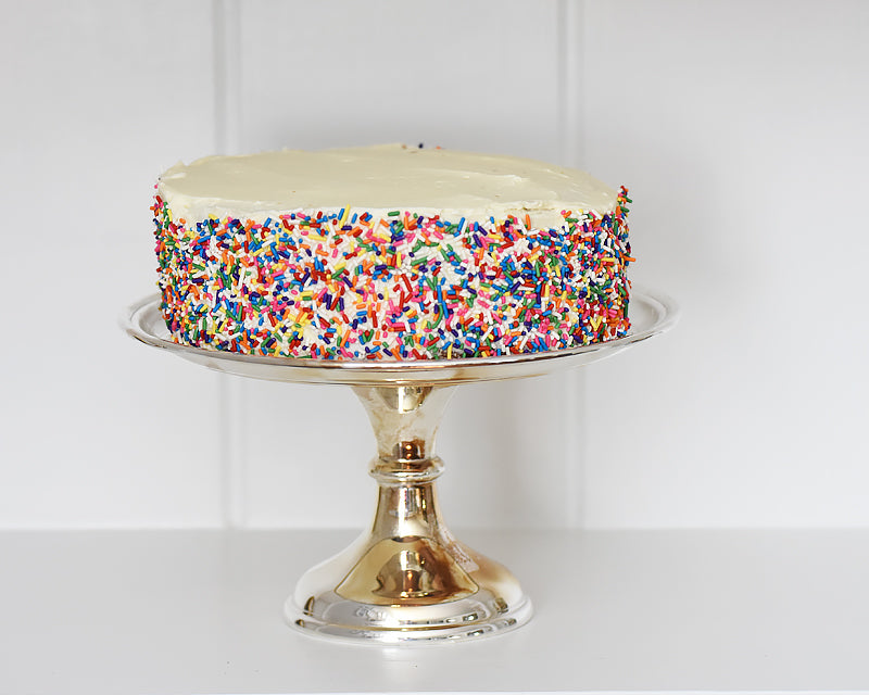 Vanilla cake with rainbow sprinkles displayed on a vintage HÔTEL Silver Cake Stand