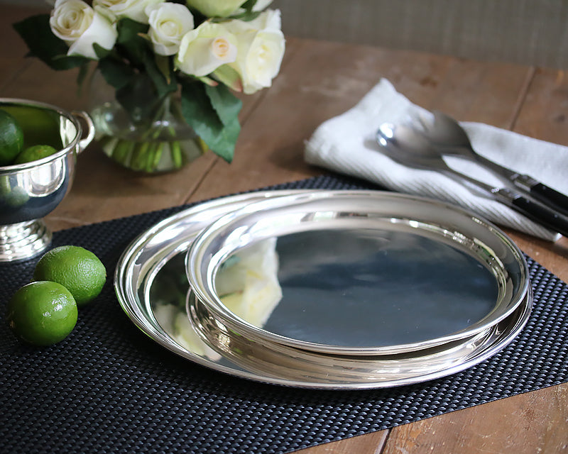 Hotel Silver round trays displayed on a black basketweave placemat next to our Hotel Silver footed bowl filled with limes.