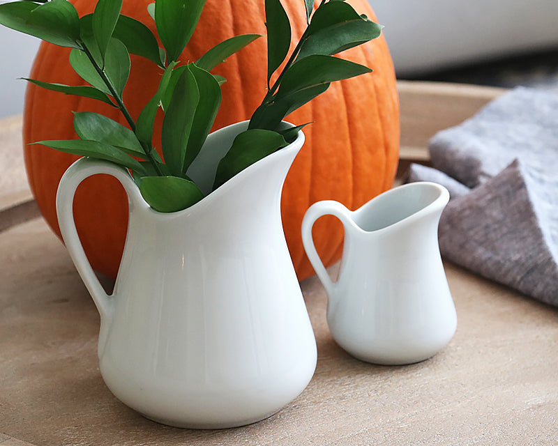 A fall setting with the milk jugs sitting side by side near a big orange pumpkin