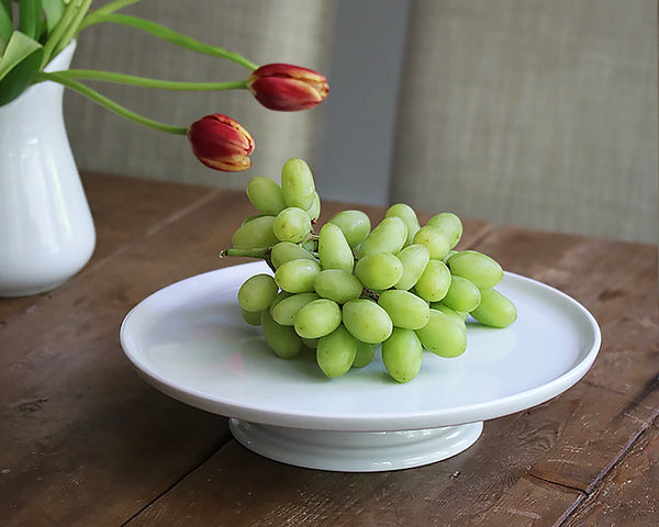 White Cake Stand by Pillivuyt sits on a wood table filled with green grapes. A great way to have the kids eat fruit!