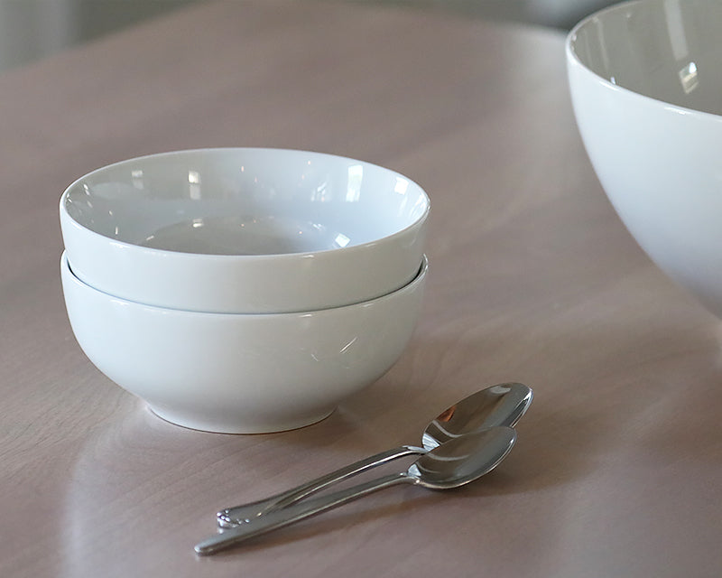 Two white cereal bowls stacked next to two spoons