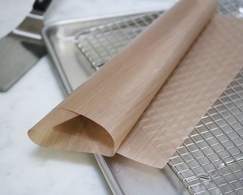 Reusable parchment sheet rolled up on a half sheet pan with a cross wire cooling rack. 