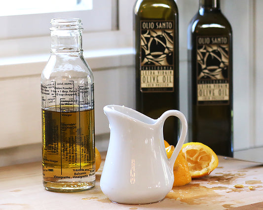 Salad Dressing bottle sits next to 2 bottles of Olio Santo Olive oil and a 9 Oz milk jug filled with lemon juice