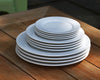 4 stacked sets of white Pillivuyt dinner plates, salads plates, and dessert plates on wooden table